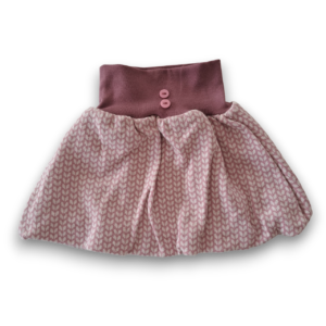 Kinder-Jupe aus roséfarbenem Baumwolljacquard mit brombeerfarbenem Bund und zwei rosa Knöpfen.