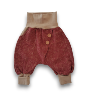 Babyhose aus rostrotem Stoff mit dezentem Muster und sandfarbenen Bündchen sowie zwei passenden Knöpfen am Bund.