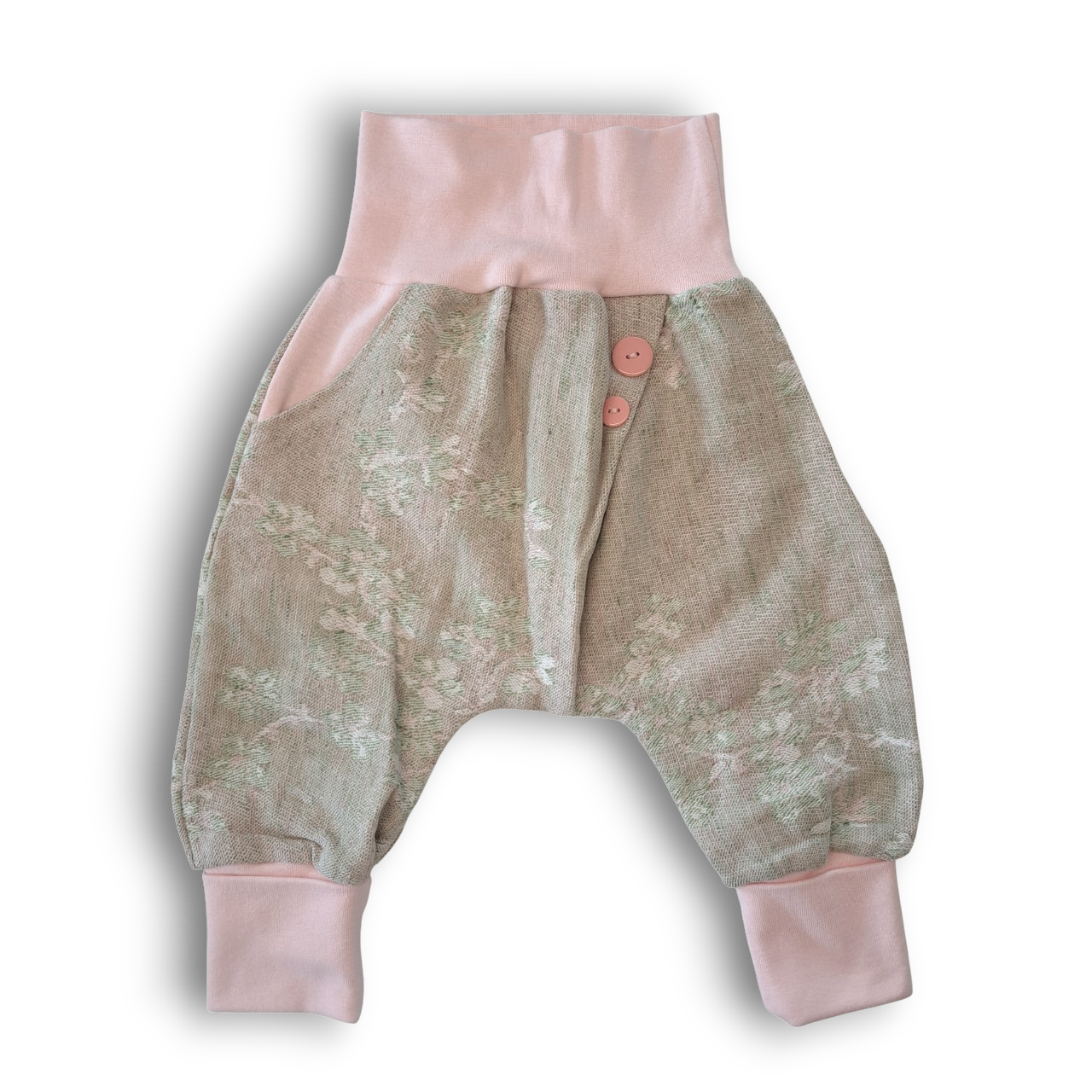 Baby-Haremshose aus beigefarbenem Stoff mit dezentem weiß-grünem Blumenmuster, rosa Bündchen und zwei rosa Knöpfen am Bund.
