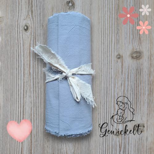 Gerolltes graues Bengkung-Belly-Binding-Tuch aus Stoff, mit einem naturfarbenen Band zusammengebunden, auf hellem Holzuntergrund, dekoriert mit Herz- und Blumen-Grafiken sowie dem Logo „Gewickelt“.