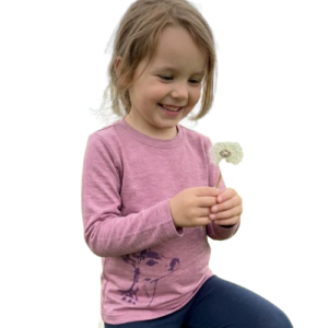Ein Kind trägt ein altrosafarbenes Kinder-Langarmshirt aus Merino-Seide mit Reh-Print und hält eine Pusteblume von heywool