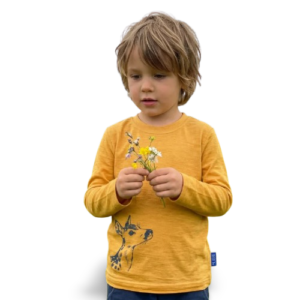Ein Kind trägt ein senfgelbes Kinder-Langarmshirt aus Merino-Seide mit Reh-Print und hält kleine Blumen von heywool